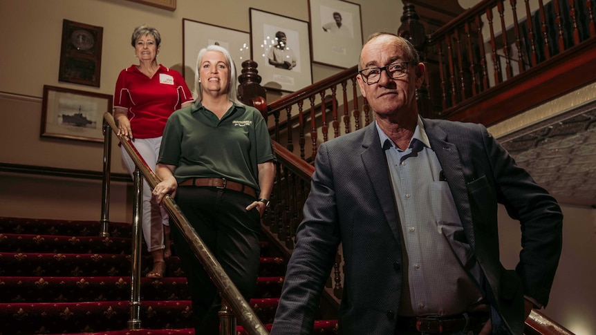 A man and two women looking at the camera, pictured standing on a staircase.