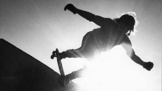 A silhouette of Bob Hastie on the lip of a skate ramp with the sun shining behind him.