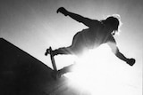 A silhouette of Bob Hastie on the lip of a skate ramp with the sun shining behind him.