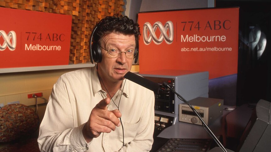 A man in a radio studio points at the camera.