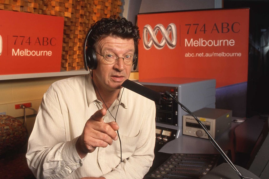 A man in a radio studio points at the camera.