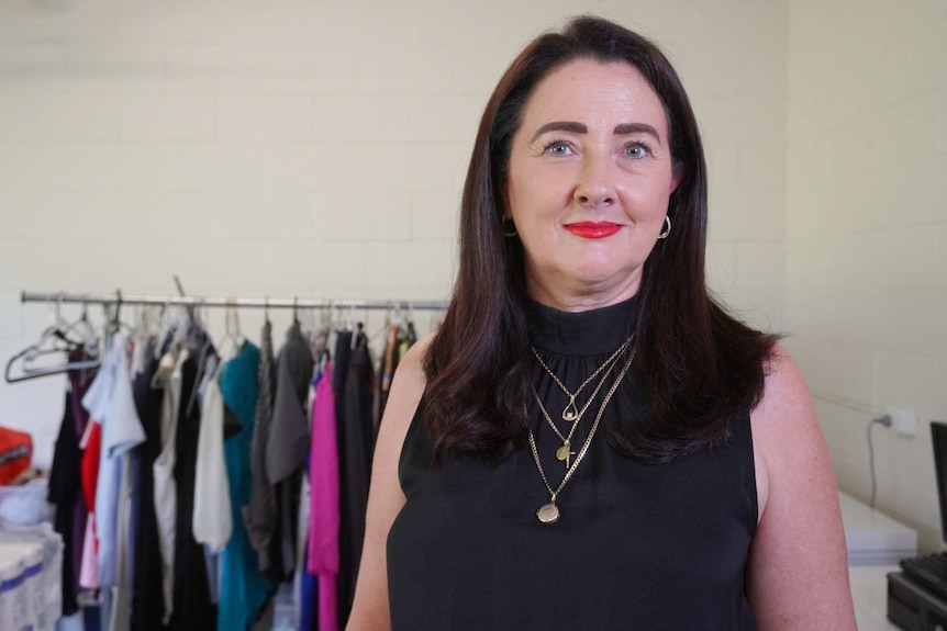 A woman smiles with a clothes rack behind her.