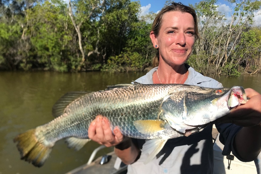 Dr Joanne Randall holds up a barramundi as she stands in a tinny.