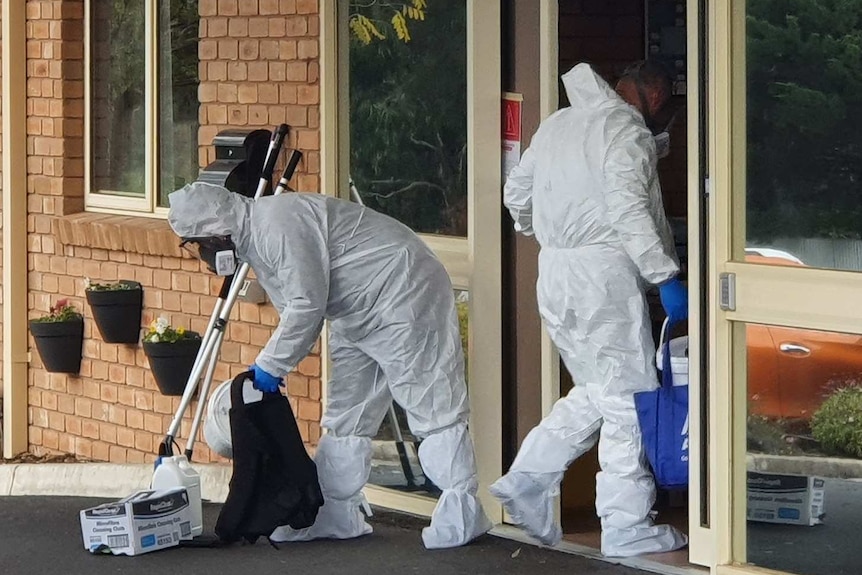 Cleaners wearing full PPE hold cleaning equipment and walk into an aged care home.