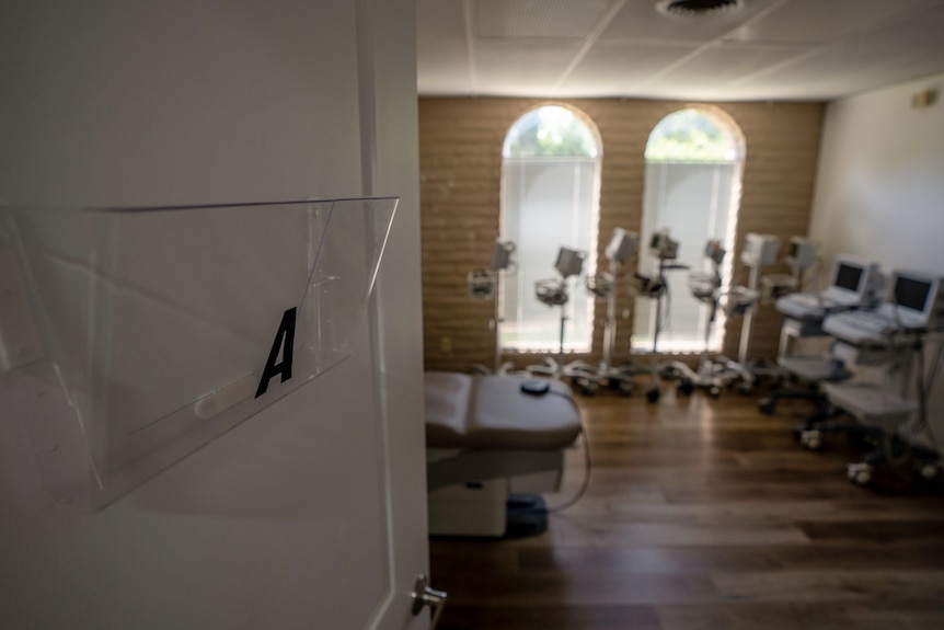 The view from an open door shows an examination table and other monitoring equipment lined up against a wall