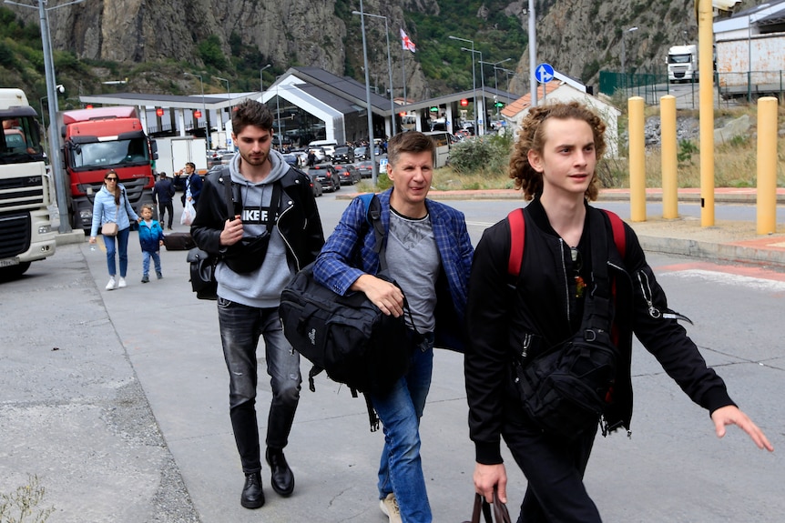 Trois hommes portant des sacs, marchent en file le long d'une route