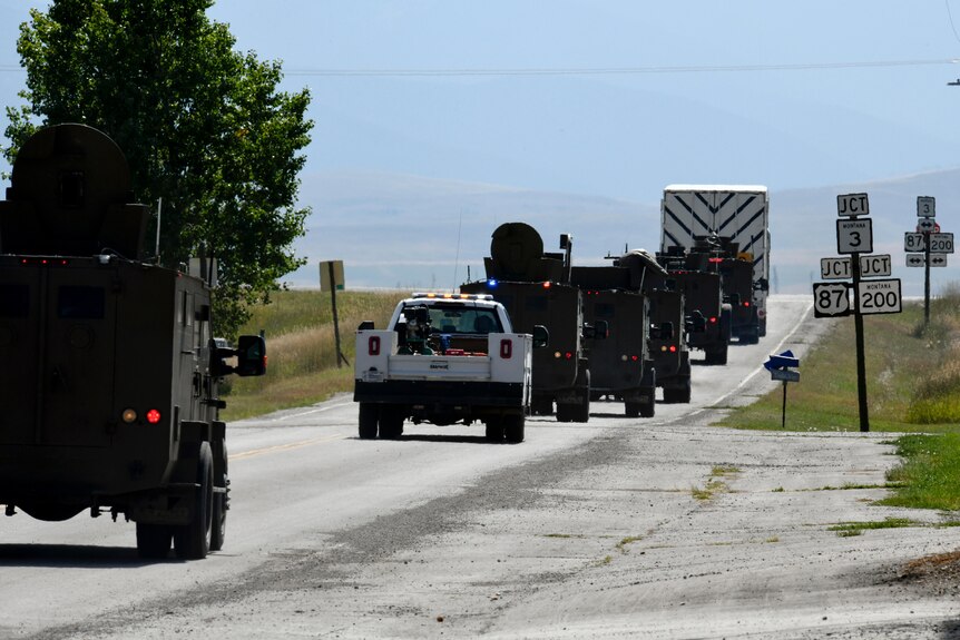 Military vehicles drive along a road in Montana as an armed escort for a nuclear warhead 