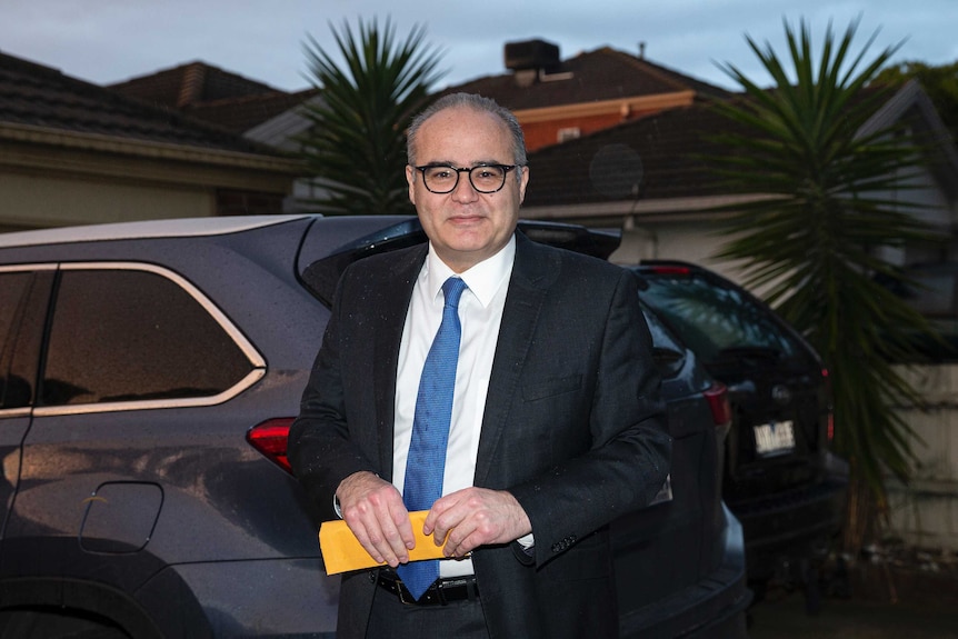 Adem Somyurek smiling but looking slightly worried while standing in front of a car.