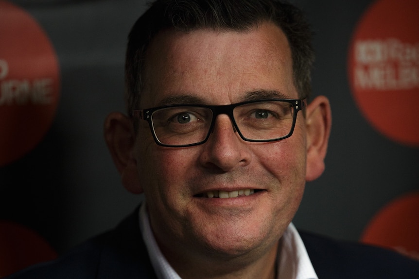 A portrait photograph of Daniel Andrews smiling, with the ABC Radio Melbourne studio behind him.