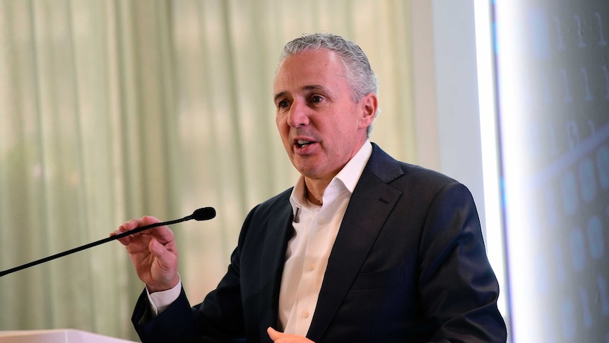 Telstra chief executive Andy Penn wears a black suit and speaks at a lectern.