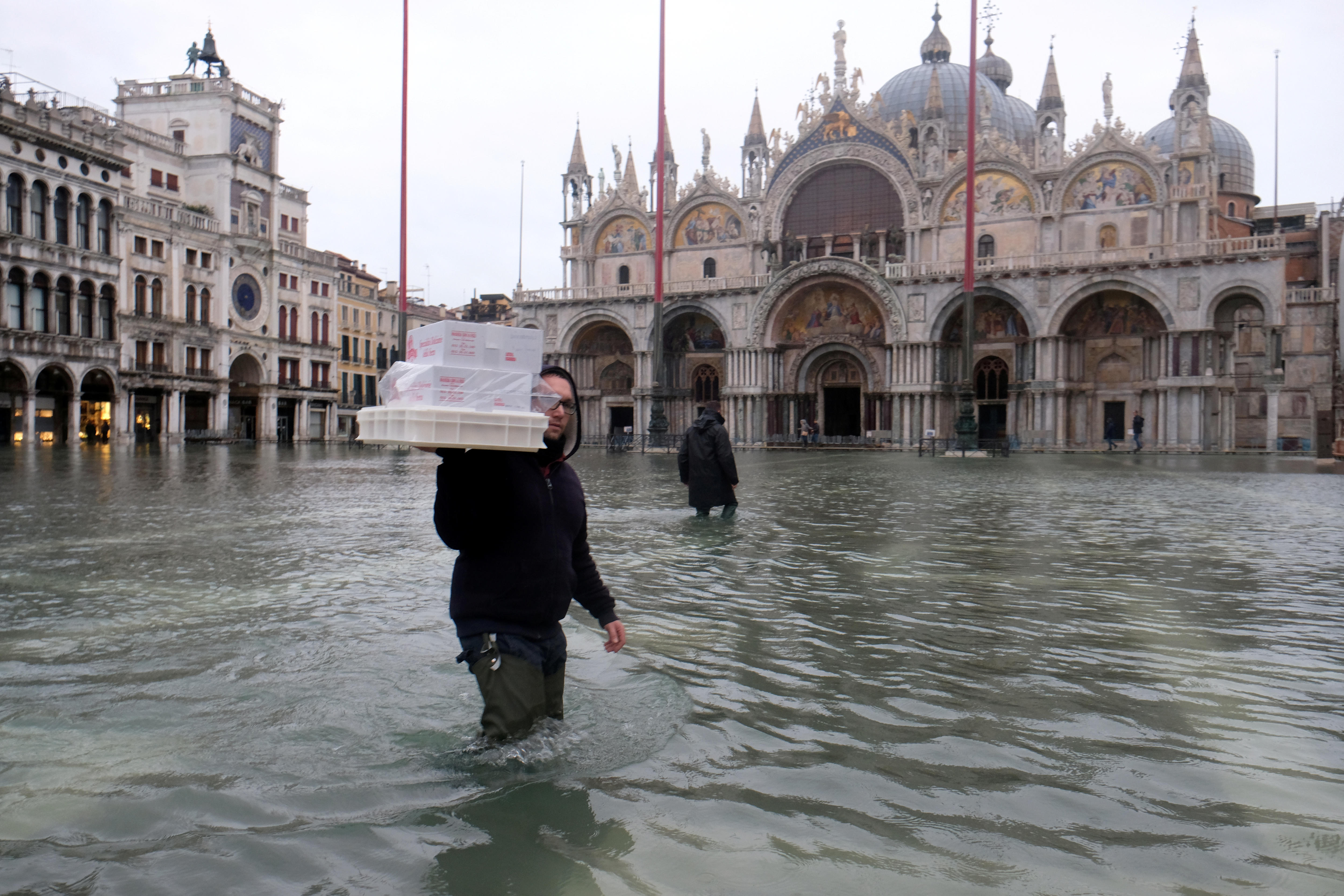 A man carrying packages in thigh-deep floodwaters.