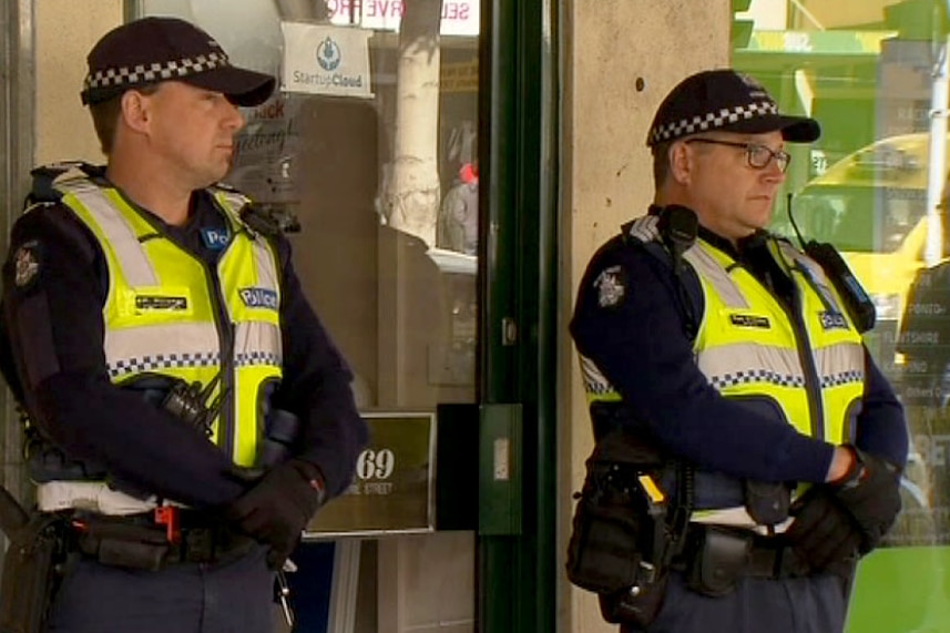 Officers stand guard outside a Geelong business raided by AFP, Victoria Police