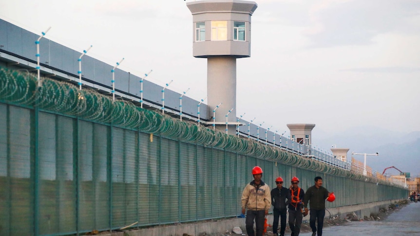 A wide shot shows watch towers and barbed wire fence around a building.