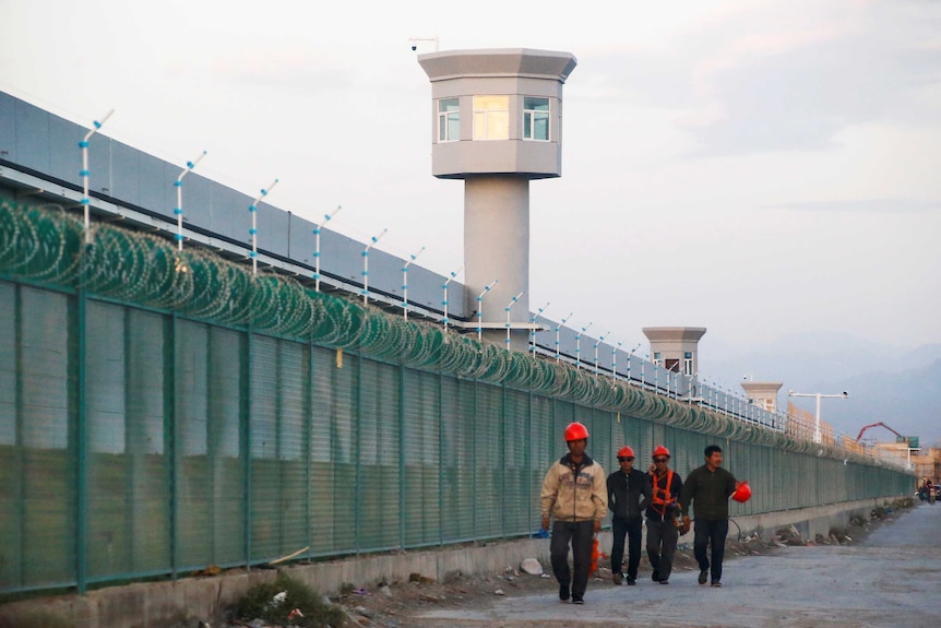 A wide shot shows watch towers and barbed wire fence around a building.