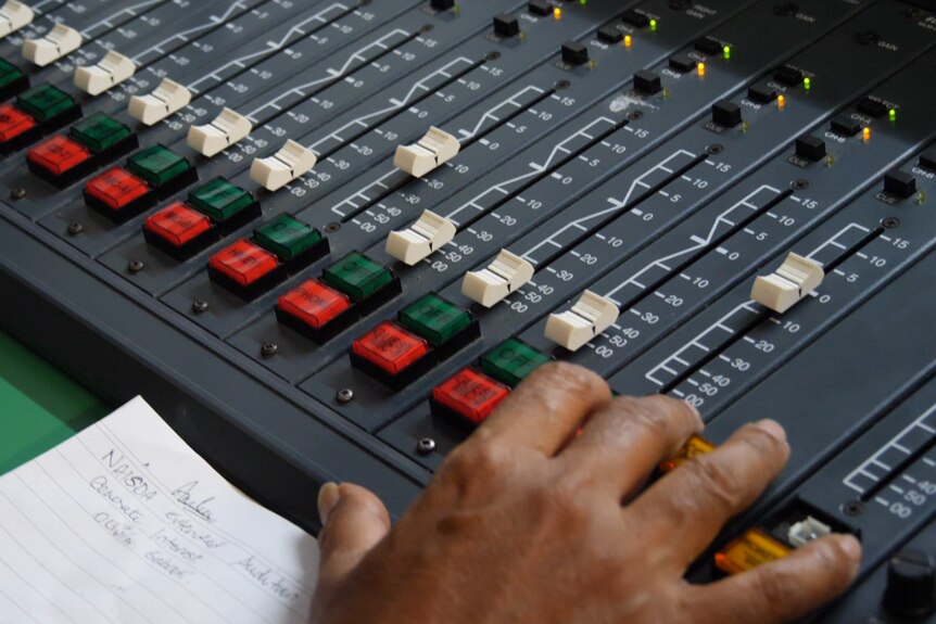 a hand on a radio desk fiddling with faders 