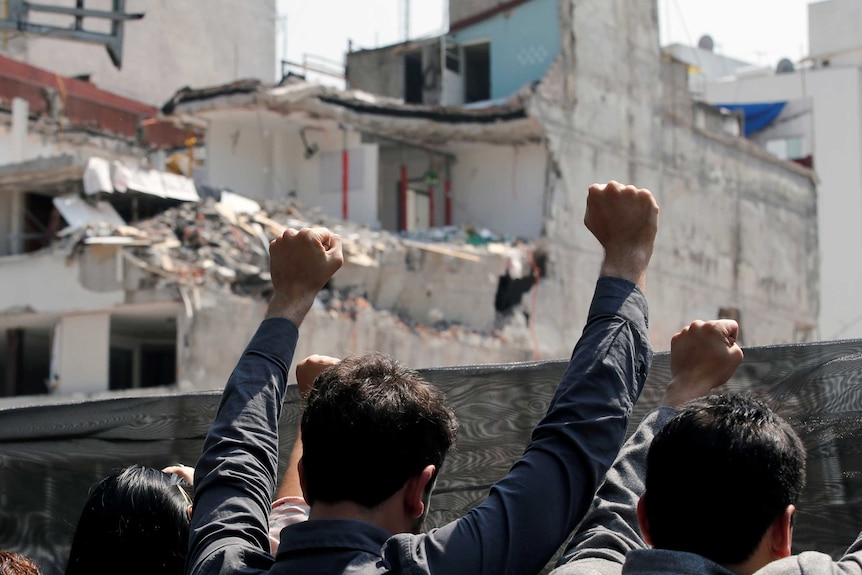 People raise hands outside a collapsed building in Condesa Mexico City