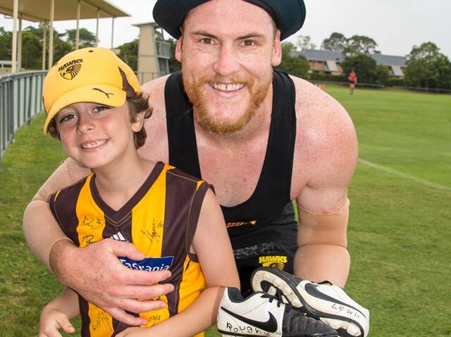 young boy and AFL player smiling holding kids boots