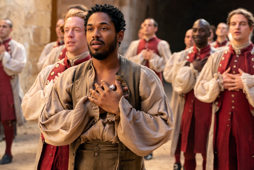 A 20-something African American man in 16th century dress stands mid-song, his hands clasped on his heart