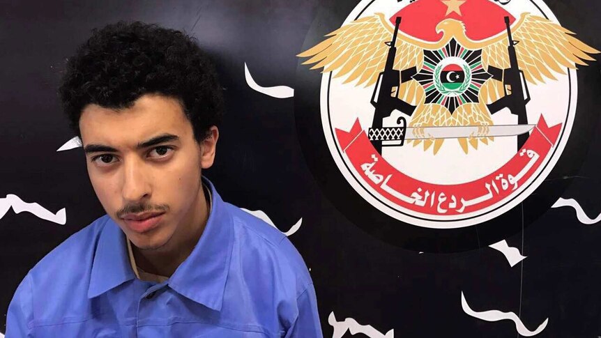 Hashim Ramadan Abedi looks at the camera while sitting in front of a flag.