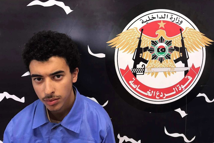 Hashim Ramadan Abedi looks at the camera while sitting in front of a flag.