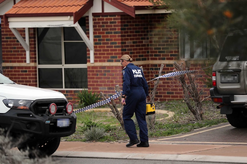 A female police forensic officer walks outside a brick house in the Perth suburb of Ellenbrook between two cars.