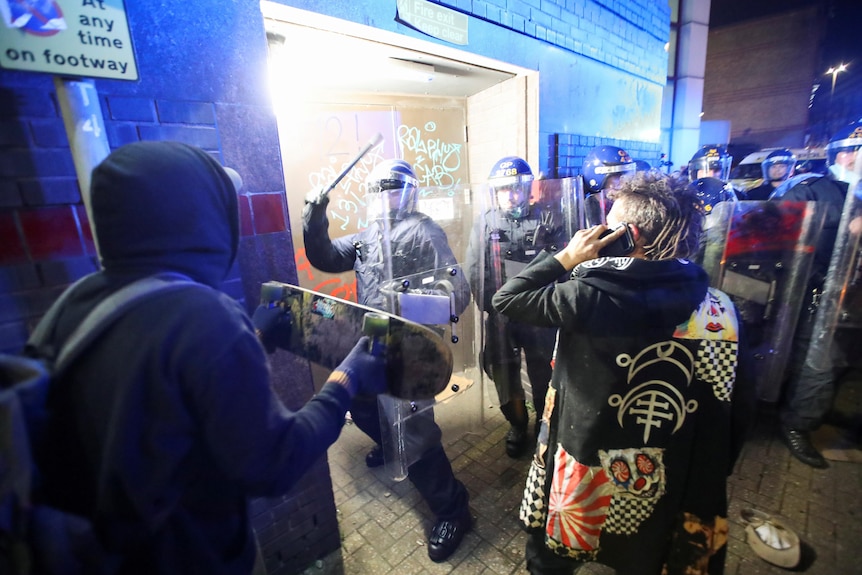 Un policier anti-émeute lève le bâton alors qu'un manifestant brandit sa planche à roulettes