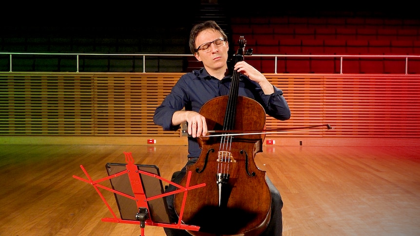 Umberto Clerici performs cello at the ABC studio with green, white and red lighting behind him