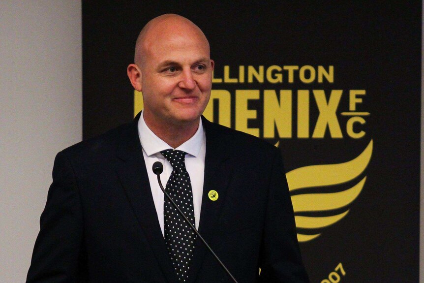 Jason Pine smiling in front of a Wellington Phoenix FC sign.