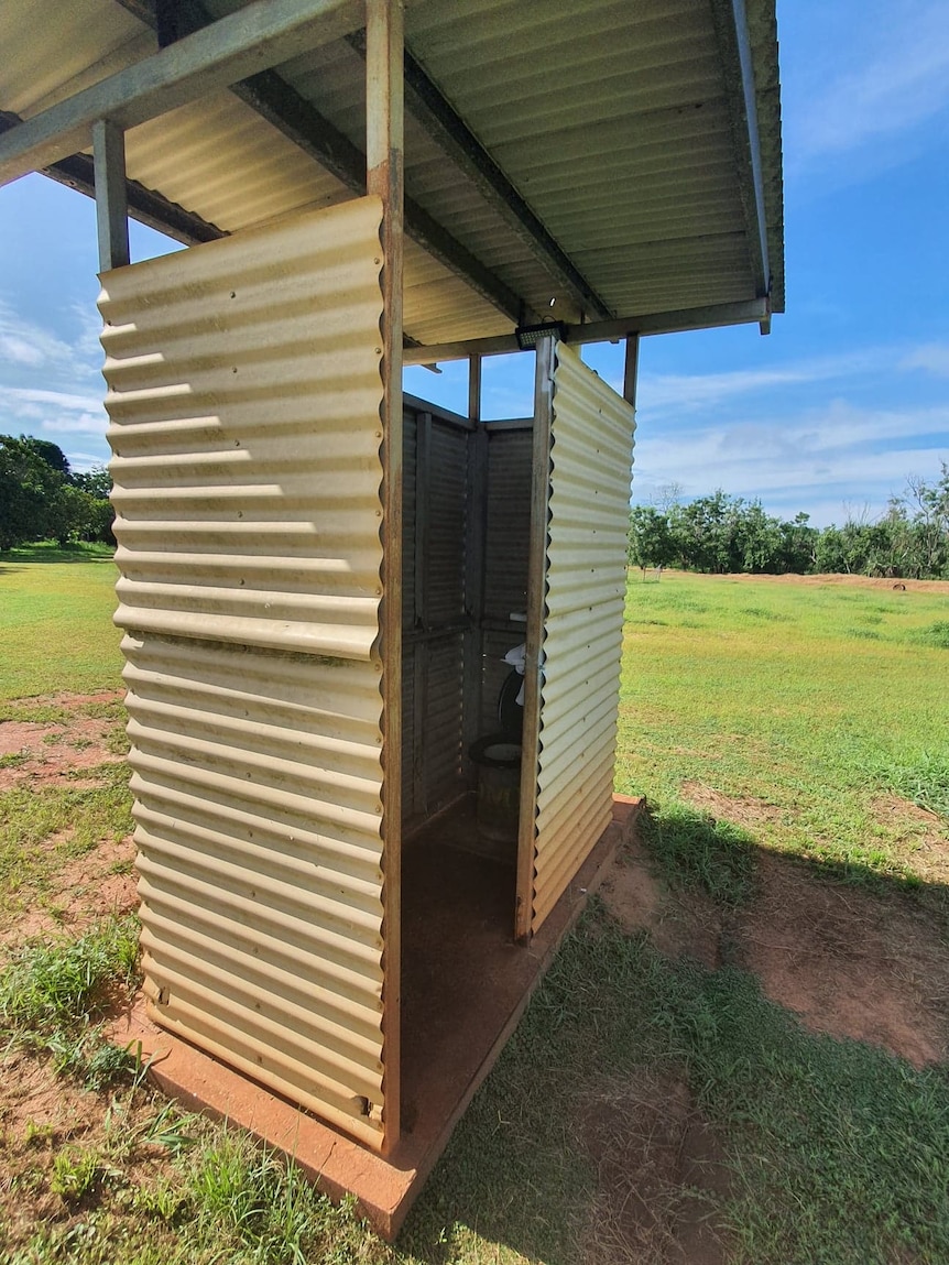 A toilet in a shed in the middle of a field.