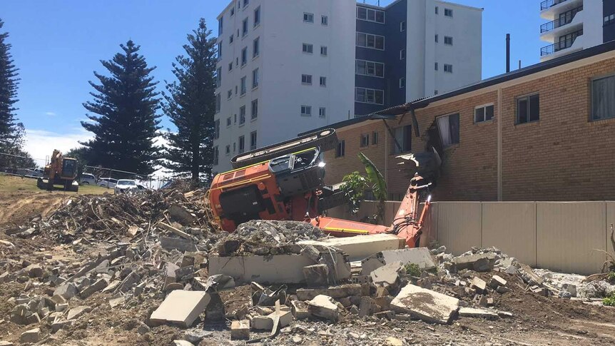 Excavator on its side on vacant block in contact with unit block