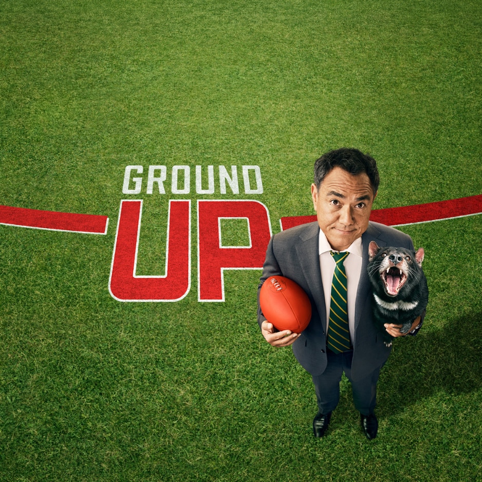 Sam Pang holding a football and a Tasmanian devil on a grass field