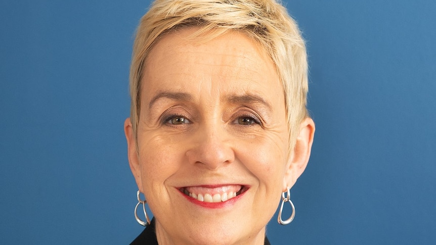 A woman with short blonde hair in front of a blue background