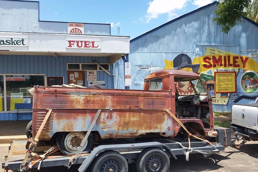 Rusty old Kombi ute on the back of a truck outside a petrol station