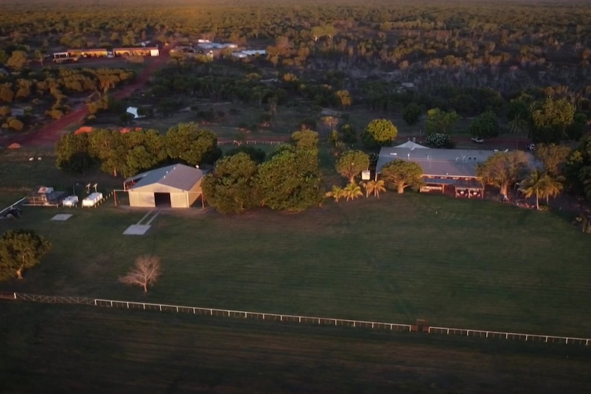 Aerial photo of outback station dwellings, sheds and homestead on green grass and trees.