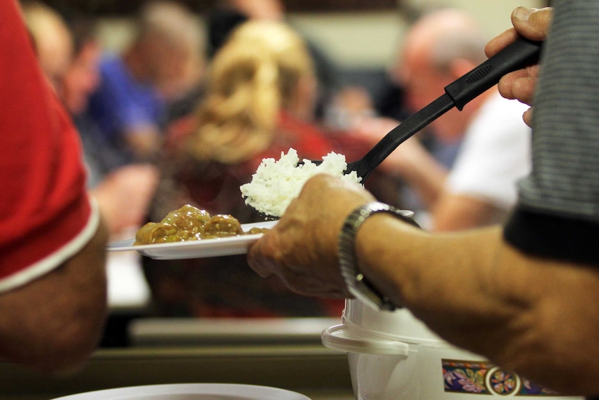 Close up on hands ladling food from pot to plate.