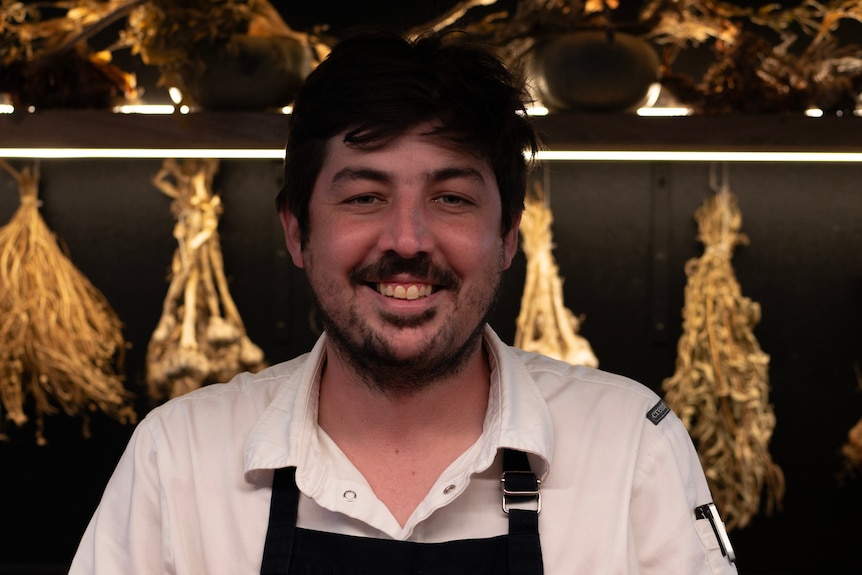 a man in a chef's apron looks directly at the camera and grins widely.
