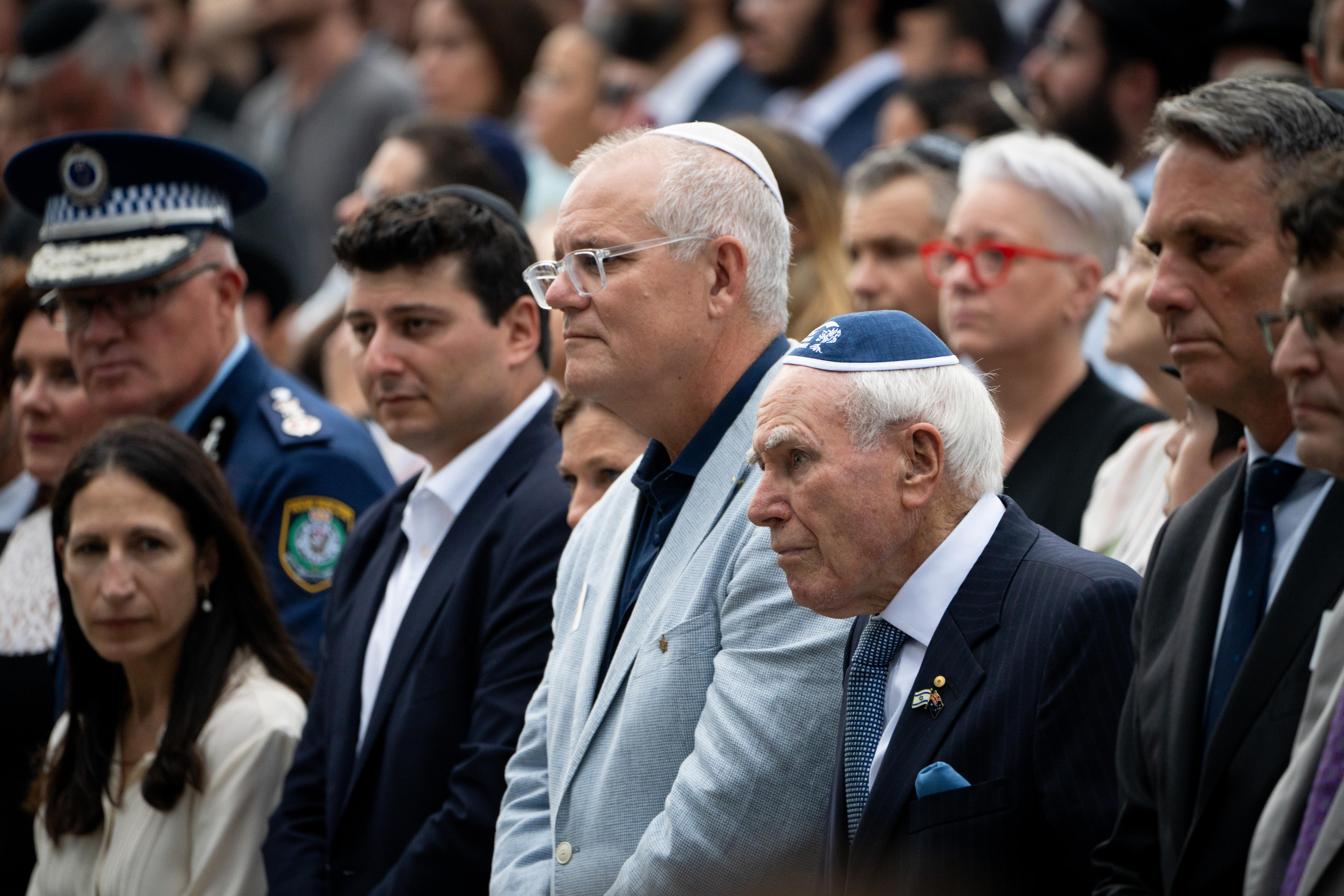 John Howard e Scott Morrison no meio da multidão com dois policiais em primeiro plano.