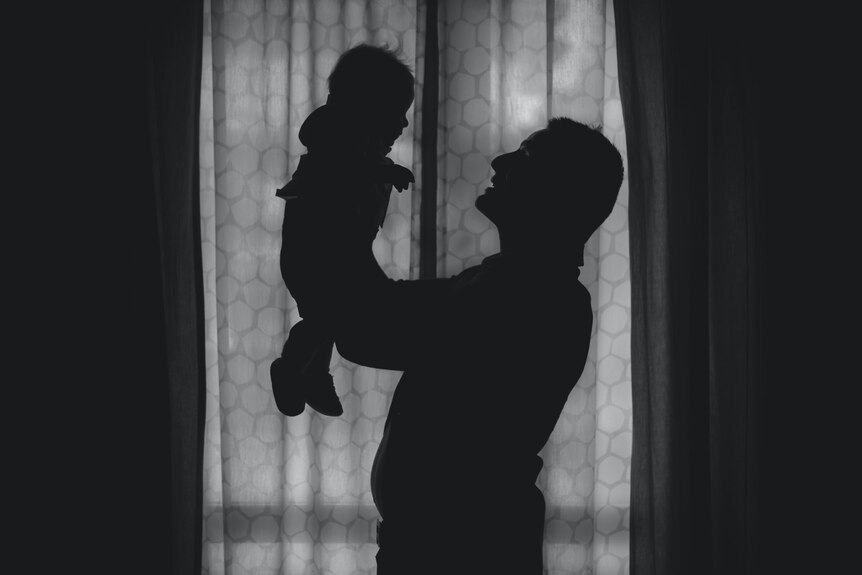 A silhouette of a man holding up a baby in front of a window