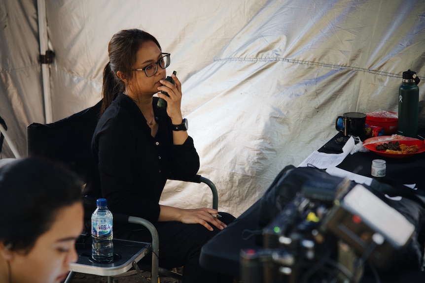 Ginanti Rona está sentada en la silla de un director en una tienda de campaña sosteniendo un walkie talkie.