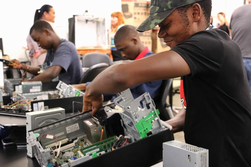 Migrant students work on building computers at a workshop at the State Library of Queensland.