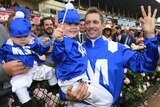 Hugh Bowman holds two children dress in Winx's colours as he holds up three fingers after winning a third-straight WS Cox Plate