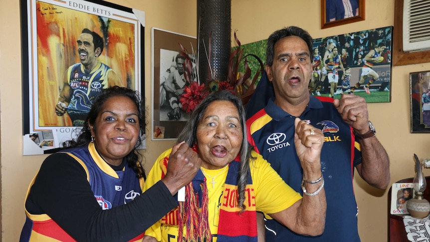 Eddie Betts family standing in front of memorabilia of the AFL star and wearing Adelaide Crows colours
