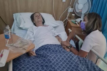 Kerry Evans sits next to her sister's hospital bed. Her sister looks unwell.