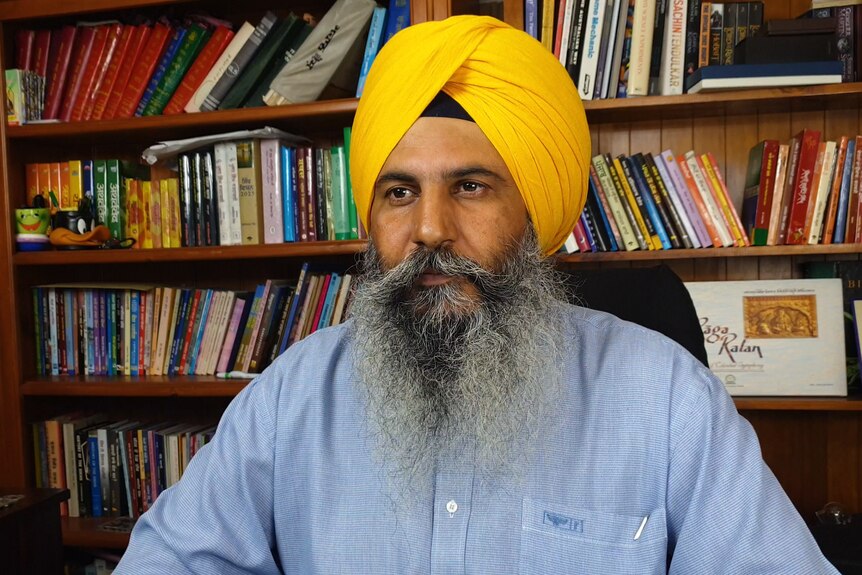 Sikh man Amandeep Singh sitting before a bookshelf 