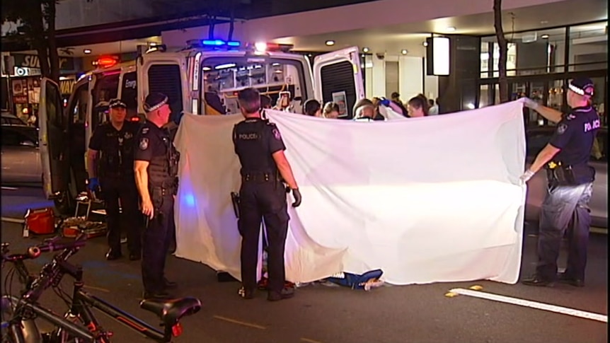 Police hold up a sheet around a teenager who is being treated by ambulance officers.
