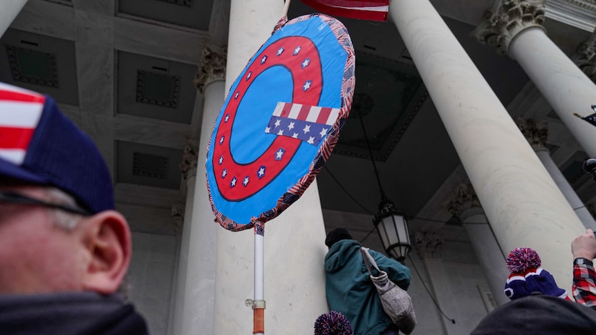 Large lollipop sign with a Q in the middle decorated in the american flag colours outside US capitol building