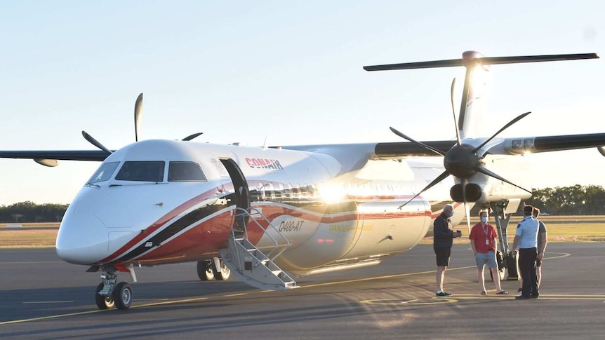 A plane sits on the tarmac with four men standing to one side of it.