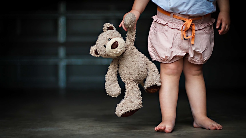 Low section of a girl holding her teddy bear.