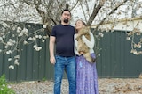 A man and woman standing together, the woman is holding a cat and smiling at the man.