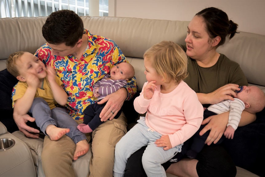 A man and a woman sitting on the couch with four small children